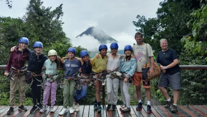 Group of people wearing helmets and harnesses standing on a platform with a cloud-covered mountain in the background.