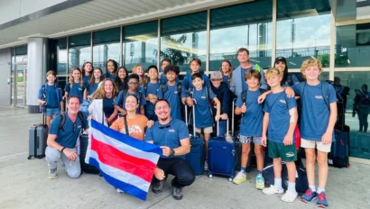 A group of people in matching blue shirts pose with suitcases and a Costa Rican flag outside a building.