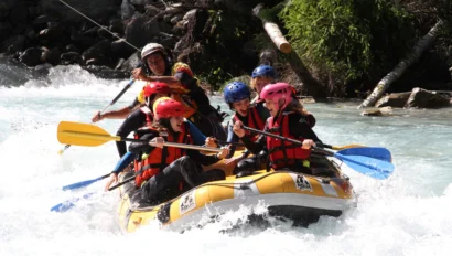 A group of people wearing helmets and life jackets are whitewater rafting on a fast-flowing river, paddling energetically through the rapids.