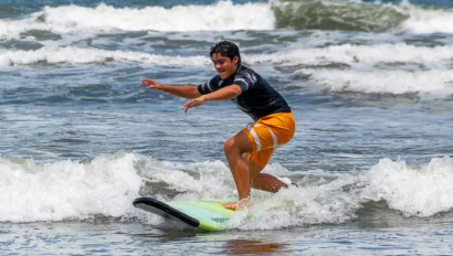 A person in orange shorts surfs on a small wave in the ocean under a cloudy sky.