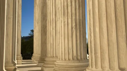 Tall marble columns with intricate capitals line a hallway, casting long shadows on the floor.