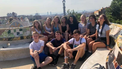 A group of young people sitting on a colorful mosaic bench with a cityscape in the background.