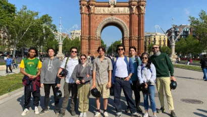 A group of people standing in front of a large archway on a sunny day, holding helmets.