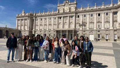 Group of people posing in front of a large, ornate historical building with a clear blue sky.
