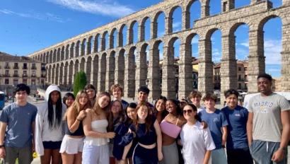 A group of people posing in front of the Segovia Aqueduct in Spain on a sunny day.