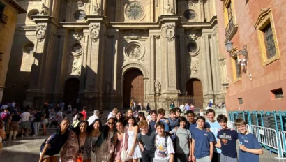 A group of people posing in front of a large, ornate historical building with tall arches and intricate details under a clear blue sky.