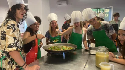 A group of people in chef hats and aprons are cooking together around a large pan in a kitchen.