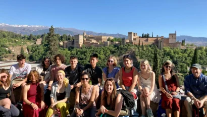A group of people sitting together with the Alhambra and mountains in the background under a clear blue sky.