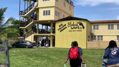 People with luggage approach a yellow building labeled "Rio Nunes Youth House Global Works" under a clear blue sky.