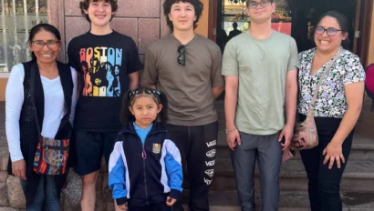 Group of five adults and one child standing in front of a building entrance, smiling at the camera.