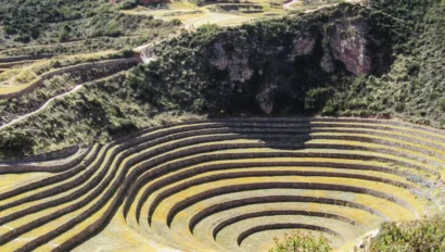 Terraced circular agricultural site set in a sunken depression with surrounding hills and paths under a clear blue sky.