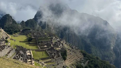 View of Machu Picchu with ancient stone structures on a hillside and misty mountains in the background.
