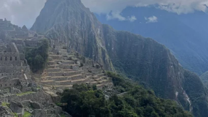 View of Machu Picchu with terraced ruins and a mountain backdrop under a cloudy sky.