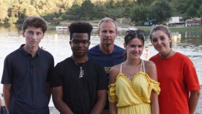 Five people standing together outdoors near a lake with trees in the background.