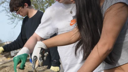 Three people wearing gloves work together to stack stones outdoors.