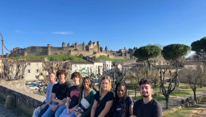 A group of people sitting on a stone ledge with a historic castle in the background under a clear blue sky.