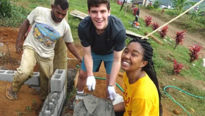 Three people working together on a construction project, handling cinder blocks and cement outdoors.
