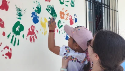 A student holding a child making a handprint on a wall.