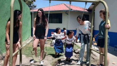 A group of students playing with children on a swing.