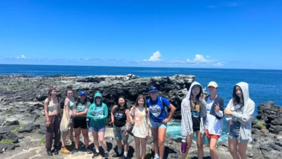 A group of people standing on rocky terrain near the ocean under a clear blue sky.