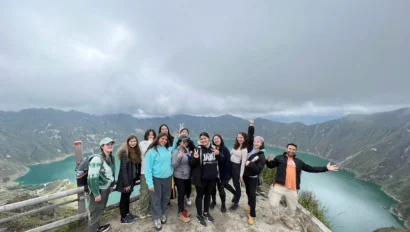 A group of people posing on a scenic overlook with a lake and mountains in the background.
