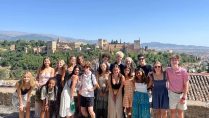 Group of young adults posing outdoors with a historic cityscape in the background on a clear day.