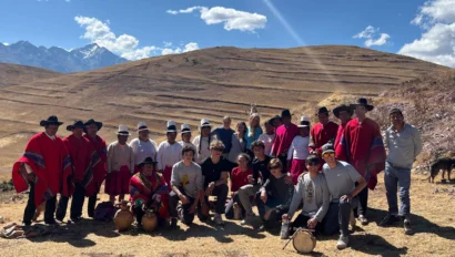 A group of people in traditional attire and casual clothes pose outdoors with mountains in the background.