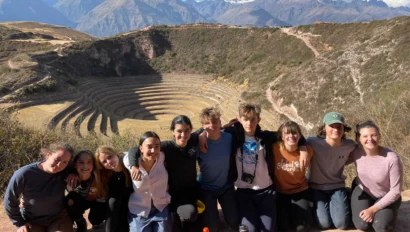 A group of people posing together in front of terraced landscape ruins with mountains in the background.