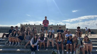 A group of people sitting on steps in front of a historic building under a clear blue sky.