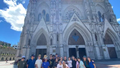A group of people posing in front of a tall, ornate cathedral under a bright blue sky.