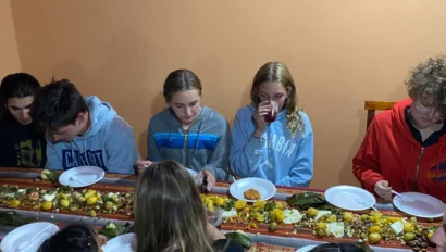 A group of people sit at a long table, eating a meal served on banana leaves.