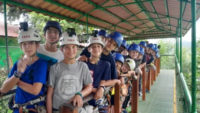 A group of people wearing helmets and harnesses stands on a platform, preparing for an outdoor adventure activity.