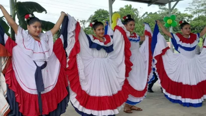 Four women perform a traditional dance in colorful, layered dresses under a canopy.