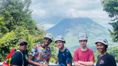 Five people wearing helmets and harnesses stand on a deck with trees and a volcano in the background under a partly cloudy sky, capturing the spirit of Costa Rica student travel.