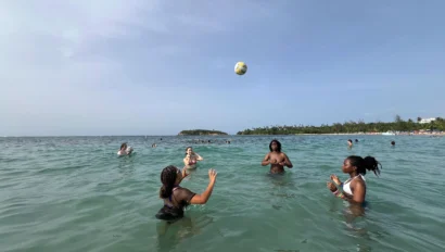 People playing with a ball in the ocean, with others swimming in the background.
