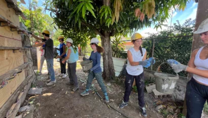 People wearing hard hats and gloves are passing buckets of material while working on a construction site outdoors.