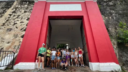 A group of people stand in front of a red historical archway with a plaque above.