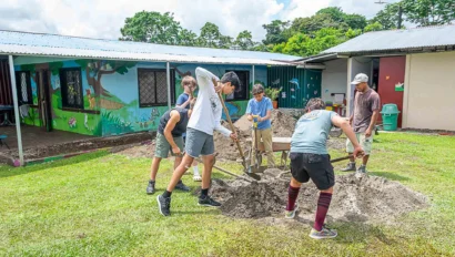 A group of people digging in a grassy area near a building with murals.