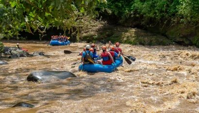 People wearing life jackets are rafting down a turbulent river surrounded by lush greenery.