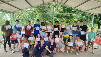 A group of people under a pavilion holding certificates and smiling. Some are holding a volleyball. Trees are visible in the background.