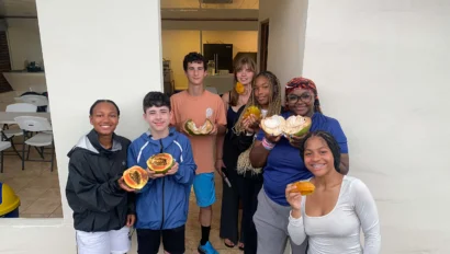 A group of six people standing outside a building, holding pieces of fruit and smiling at the camera.