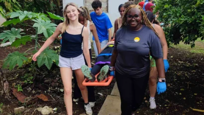 A group of students and medical professionals, during a medical study abroad program in Costa Rica, carrying a person on a stretcher along a garden path, with greenery and a small shed in the background.