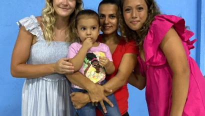 Four people pose in front of a blue wall; an adult holds a young child, with two others—perhaps sharing stories of student travel to Costa Rica—standing on either side, all looking at the camera.