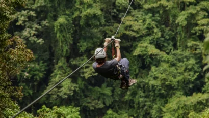 A person wearing safety gear rides a zipline over a dense, green forest during a student travel program by Global Works.