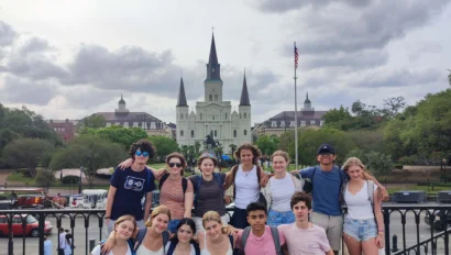 A group of people posing in front of a historic church with spires, under a cloudy sky.