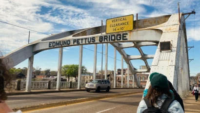 Students walk across the Edmund Pettus Bridge in Selma, Alabama on a partly cloudy day, with a car driving beside them—an inspiring scene for a civil rights school trip.