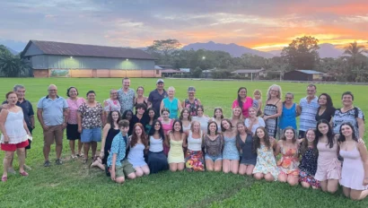 A large group of people posing on a grassy field at sunset, with a backdrop of buildings, trees, and mountains.