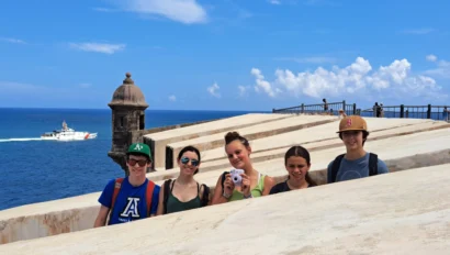 Five people standing on a stone structure by the sea with a distant boat on a sunny day.
