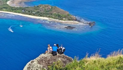 Three students sitting on a rock overlooking the ocean.