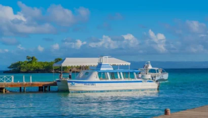 Two boats are docked at a wooden pier on clear blue water, perfect for a school travel program adventure, with a small island and a cloudy sky visible in the background.